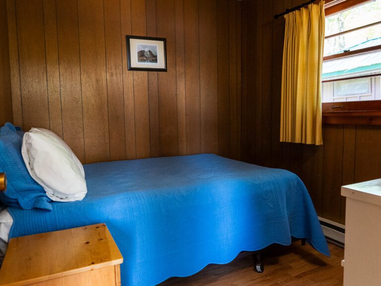 Wood-panelled bedroom with blue bedspread and yellow curtains