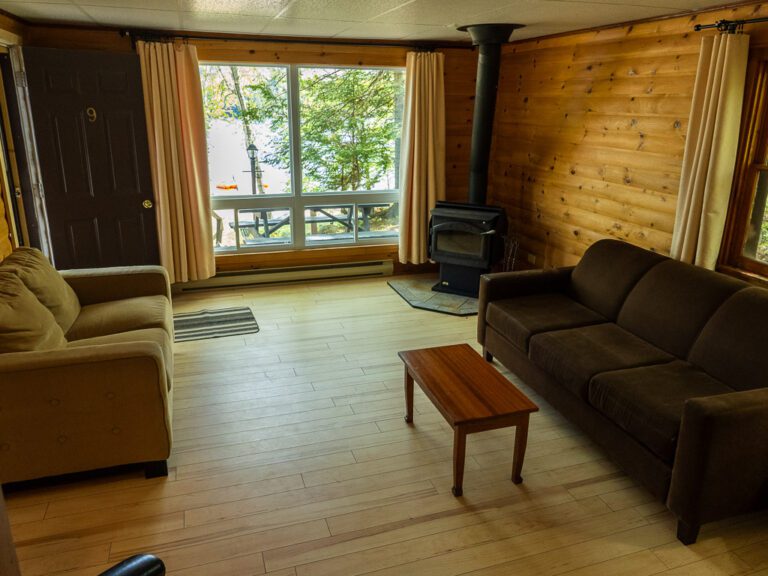 View of cozy cottage living room, looking towards fireplace and large windows